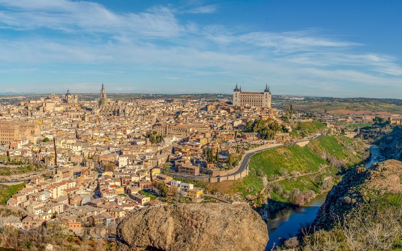 A wide angle photo of Toledo in Spain taken across the Tagus with the Toledo alcazar and cathedral pointing above the skyline.