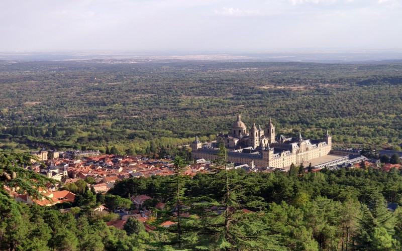 A wide angle photo looking down to the Monasterio del Escorial surrounded by forest