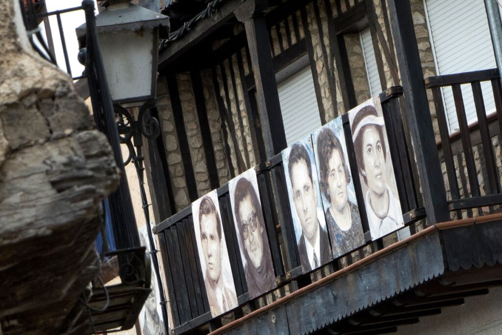 Portraits of people are displayed on a rustic balcony in Mogarraz, Spain, showcasing the town's unique artistic tradition.
