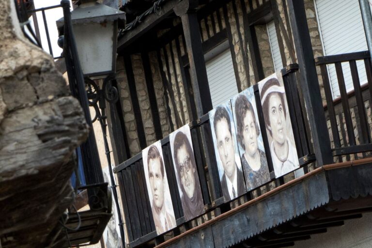 Portraits of people are displayed on a rustic balcony in Mogarraz, Spain, showcasing the town's unique artistic tradition.