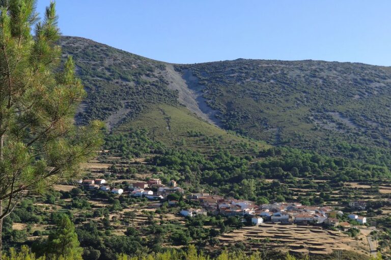 The village of Monsagro nestled in a lush valley, surrounded by terraced fields and green hills under a clear blue sky.
