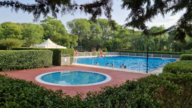 People enjoying a swim at piscina municipal Serradilla del Arro, surrounded by lush greenery and a small round pool in the foreground.