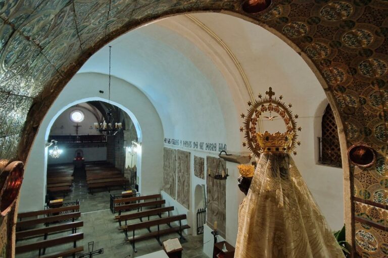 Interior of a church at La Peña de Francia, featuring a statue of the Black Madonna with a crown, overlooking wooden pews and ornate walls.
