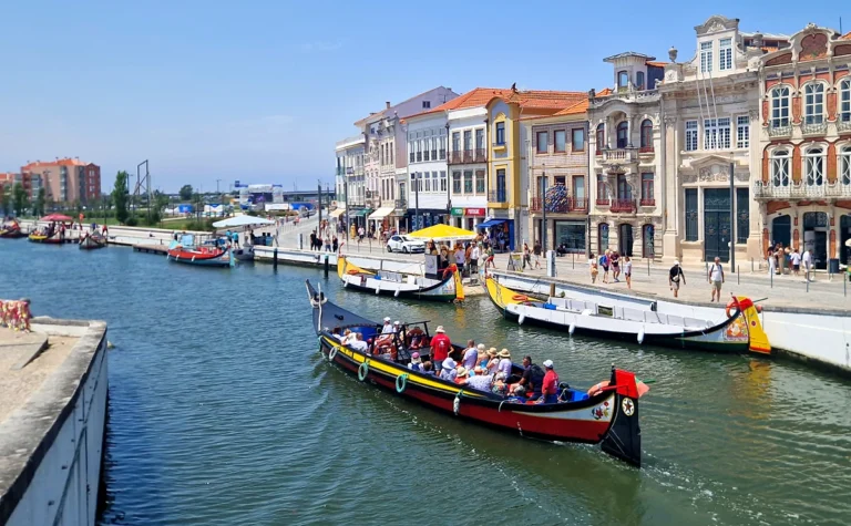 A vibrant scene along the Aveiro canal central, featuring colorful boats and historic buildings with people enjoying a sunny day.