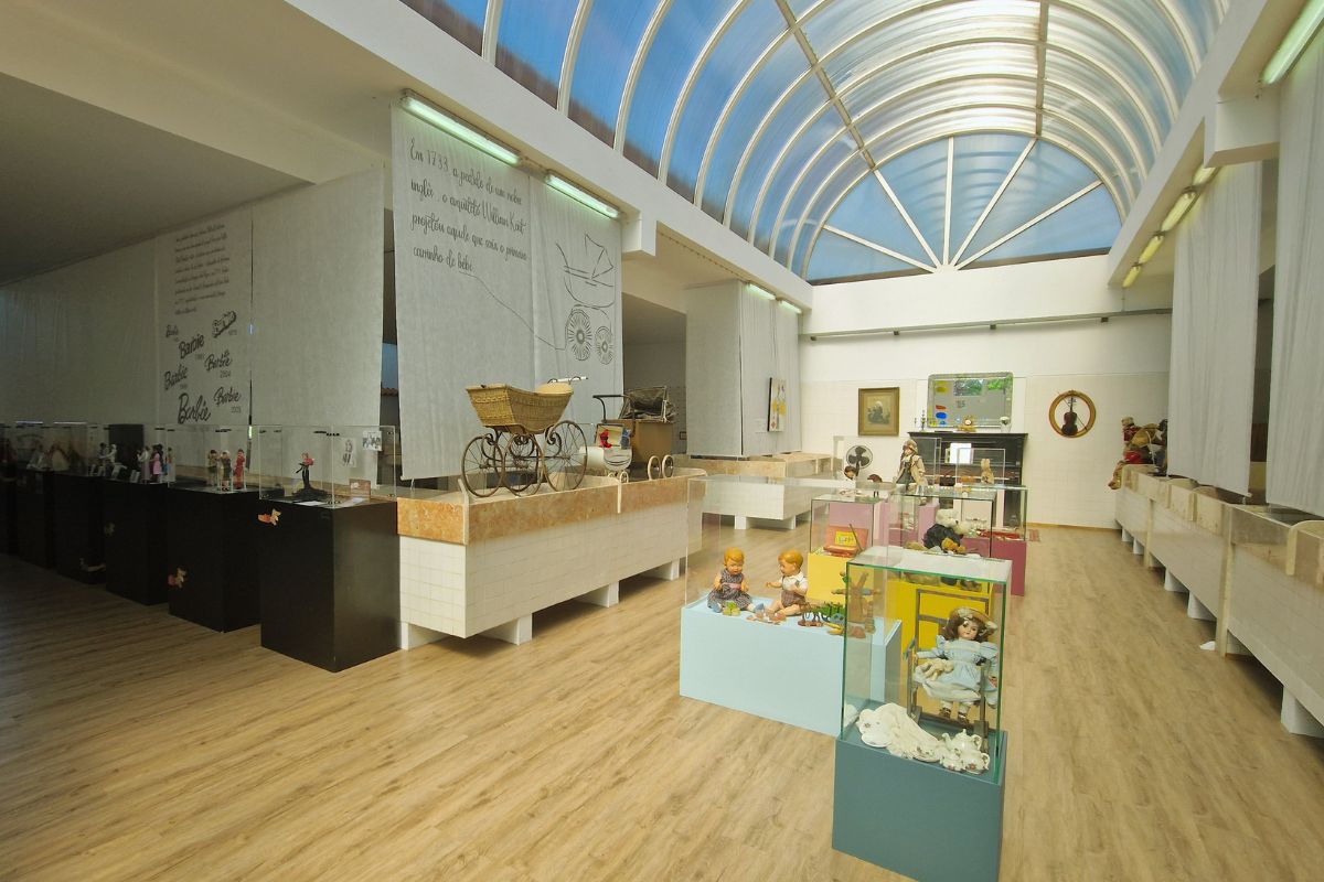The Museu do Brincar Vagos features a bright, spacious room with vintage toys and displays under a curved glass ceiling.